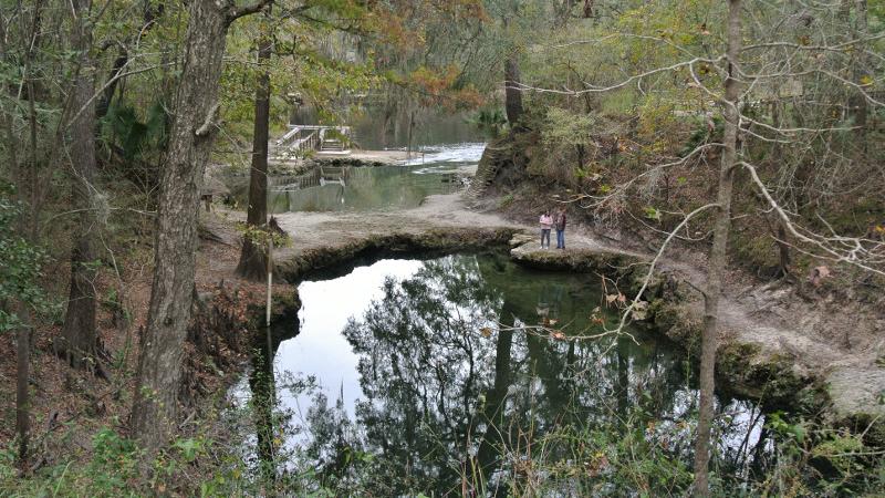 Two peope stand on an outcropping in the spring, next to a unique land bridge.